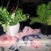 Small white mesh closet fragrance sachets from The Dewy Petal, displayed on a rose-patterned surface with green botanical plants and a dark background.